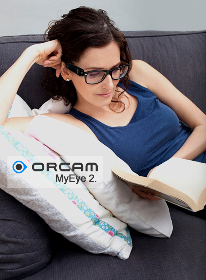 Banner-Orcam02 Mulher sentada lendo um livro com o Dispositivo OrCam MyEye 2. acoplado em seu óculos