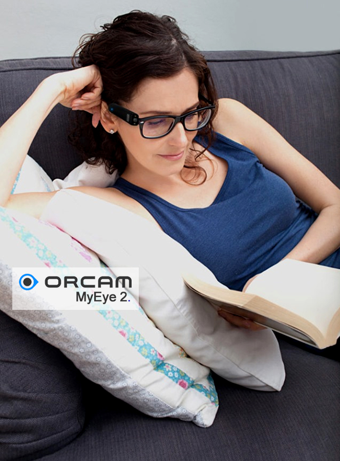 Mulher sentada lendo um livro com o Dispositivo OrCam MyEye 2. acoplado em seu óculos