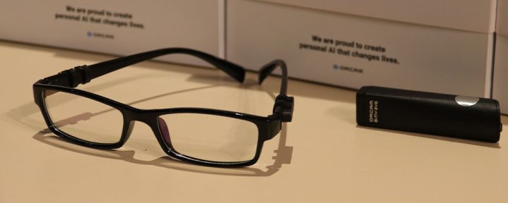 Dispositivo OrCam MyEye e uma armação de óculos estão em cima de uma mesa - Mais Autonomia
