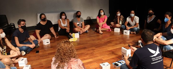 Em um palco de teatro, diversas pessoas estão sentadas em um círculo, observando o treinamento de um profissional da Mais Autonomia - Mais Autonomia