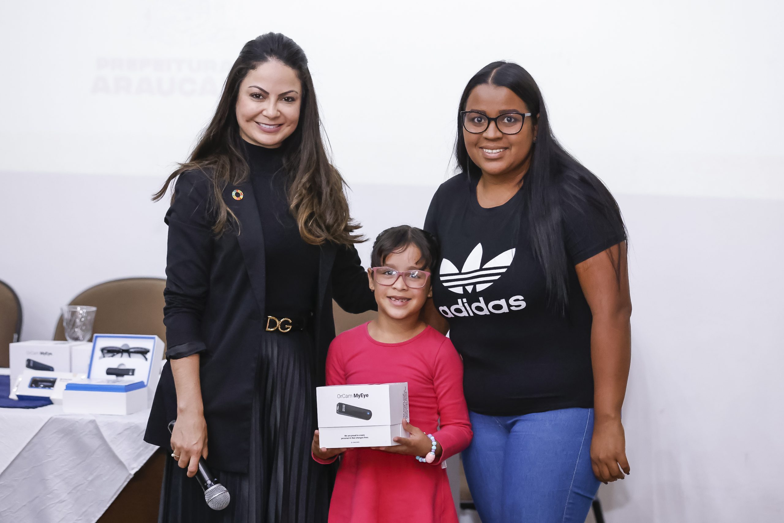 #PraTodosVerem: na imagem podemos ver a criança Alexyah recebendo o Orcam MyEye ao lado de sua mãe Deborah e Leonice Lacerda