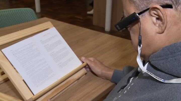 Anastácio Braga, de 69 anos, lendo um livro com o auxilio do dispositivo OrCam my eye 2.0 dentro da Biblioteca Pública do Paraná