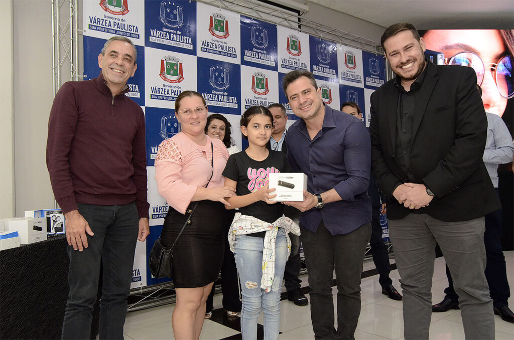 #PraTodosVerem: Na foto, podemos ver uma criança sorrindo e recebendo seu dispositivo OrCam MyEye pelas mãos do prefeito Rodolfo Braga, todos felizes